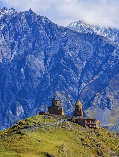 Tatev Monastery perched on green hillside with snow-capped mountains in background, Georgia
